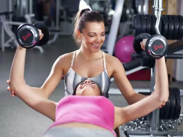 personl trainer spotting woman lifting dumbbells